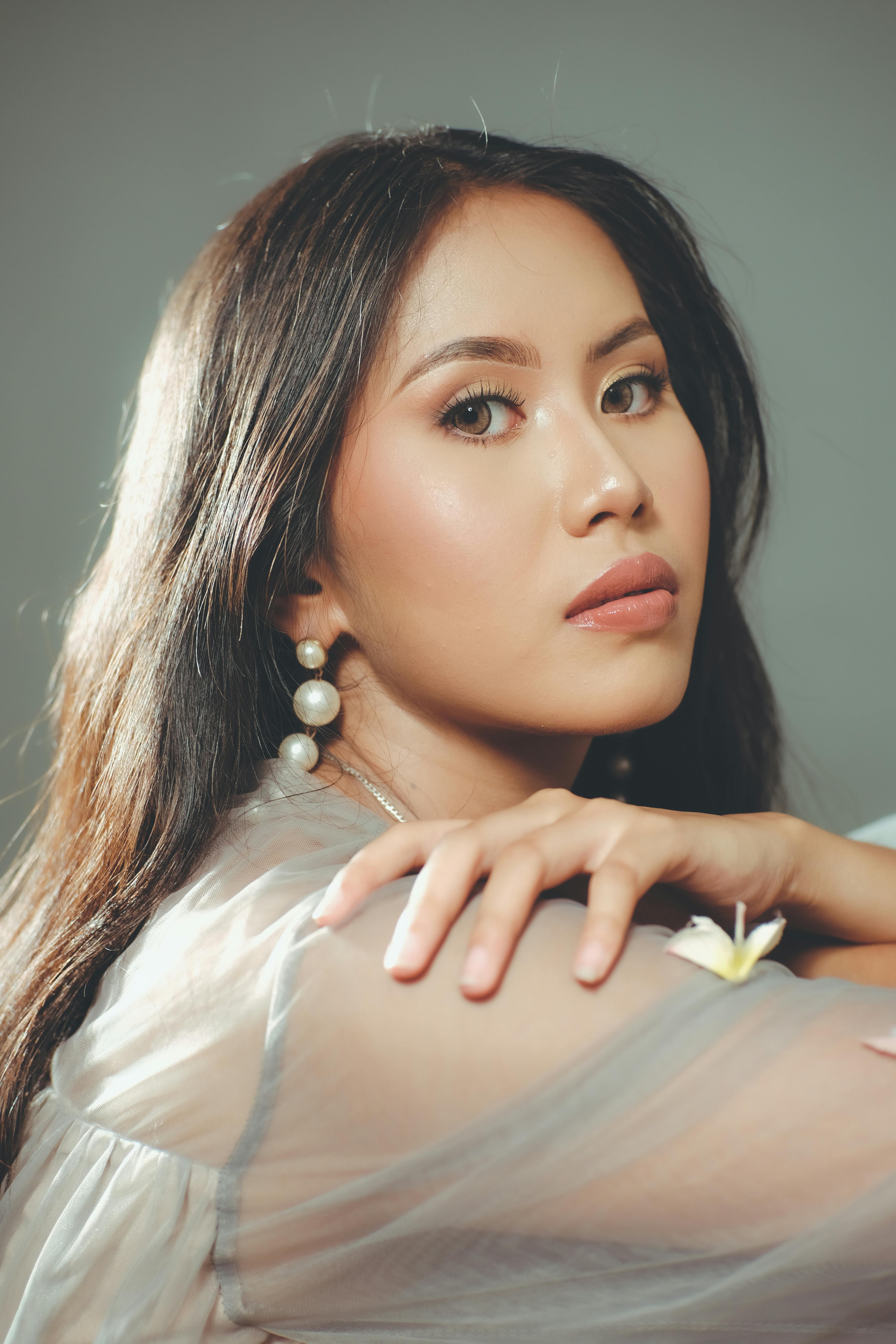 Stylish woman wearing pearl earrings poses gracefully in soft lighting.