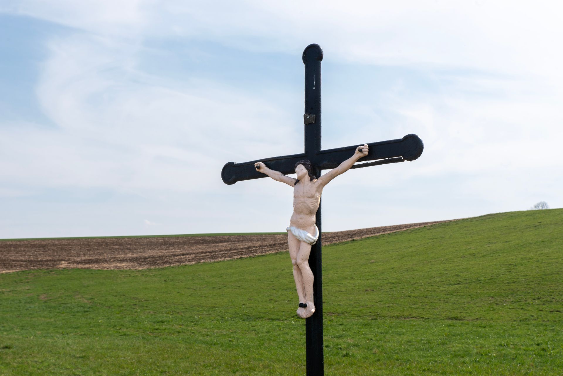 Outdoor crucifixion scene with a cross on a grassy hillside under a clear blue sky.
