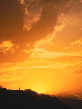 Dramatic golden sunset with clouds over hills, creating a serene and vibrant sky.