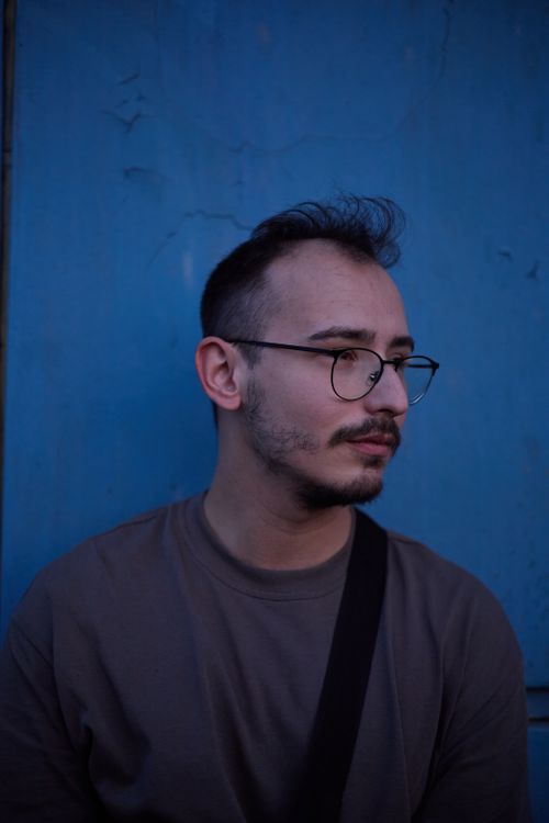 Free Young man wearing glasses, standing against a blue wall in Istanbul. Moody and artistic portrait. Stock Photo