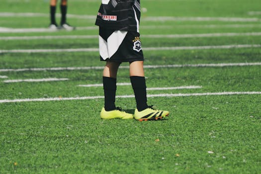 Close-up of a child's legs in soccer gear on a vibrant green football field.