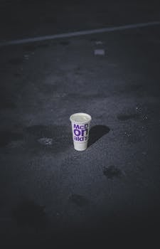 A solitary McDonald's cup sits on a deserted, dark street under night shadows.