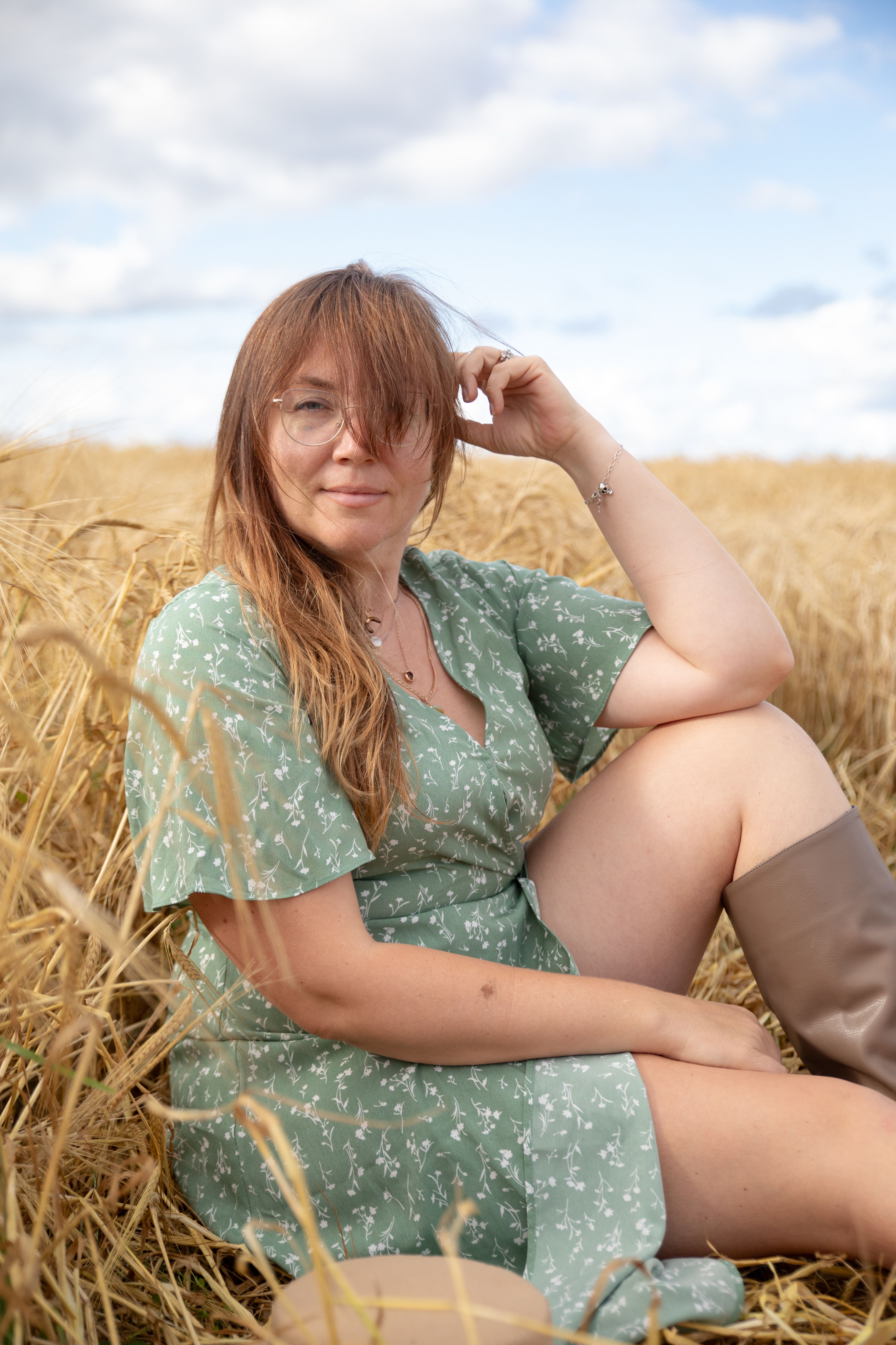 A woman in a green dress sitting in a wheat field under a bright sky, enjoying the sunshine.