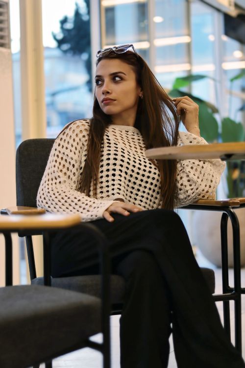 Free Relaxed woman in a coffee shop wearing a white sweater and black pants, enjoying a tranquil indoor atmosphere. Stock Photo