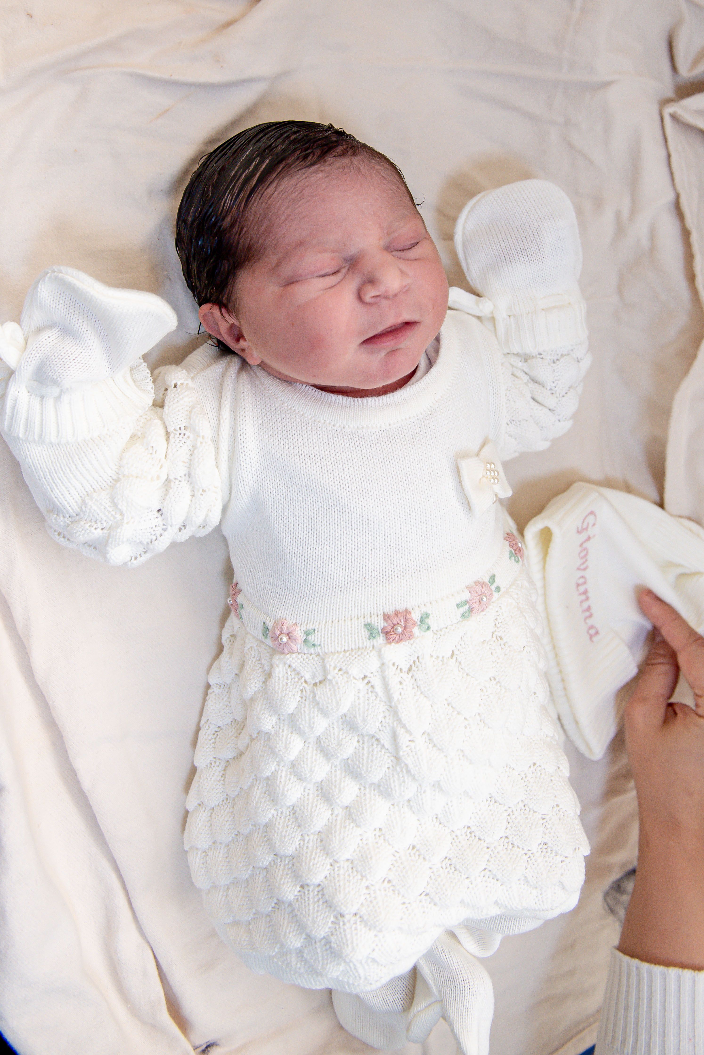 Sleeping newborn baby in a white knit outfit with floral accents, captured indoors.