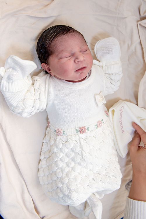 Free Sleeping newborn baby in a white knit outfit with floral accents, captured indoors. Stock Photo