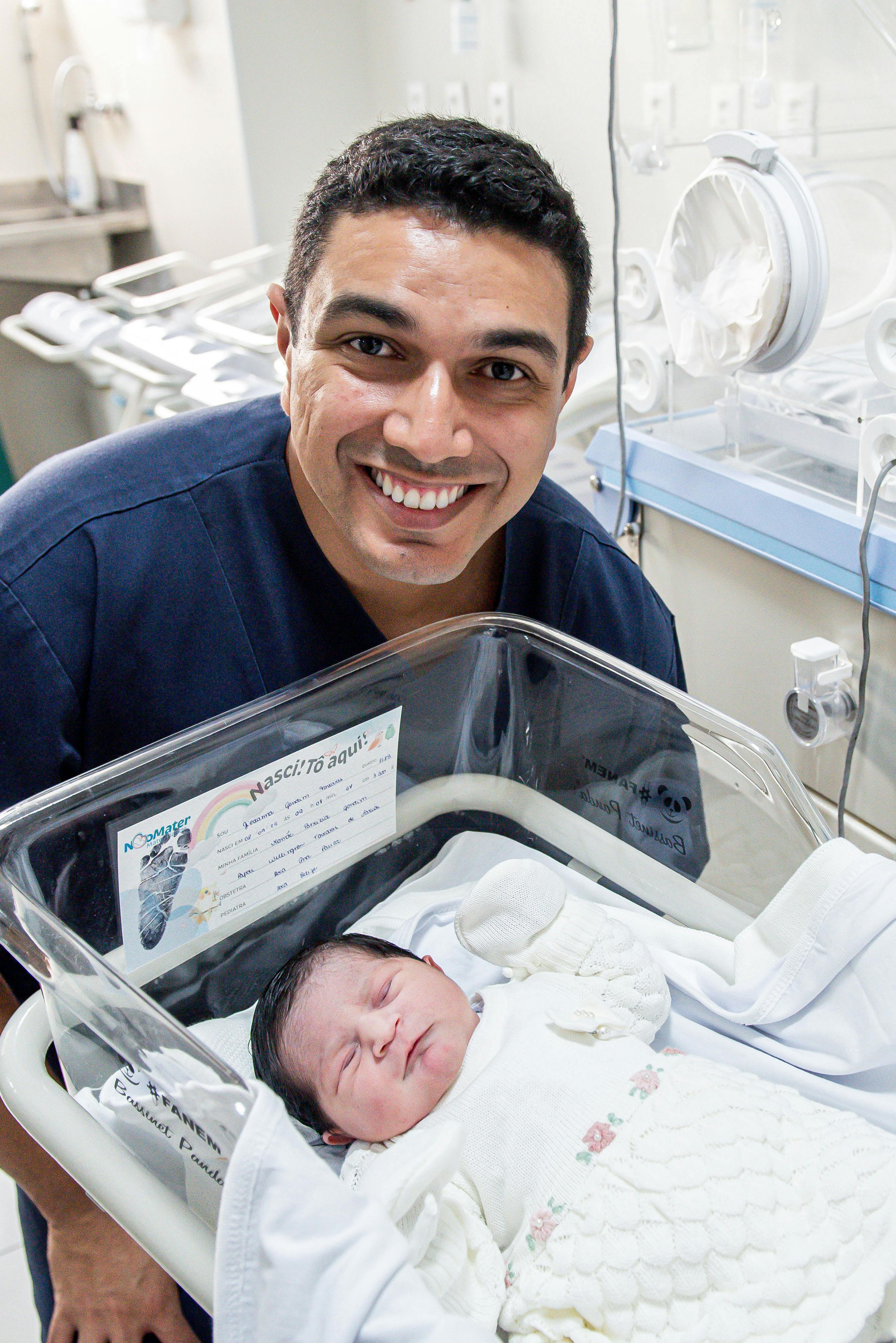 A proud nurse poses with a newborn baby in a hospital nursery setting.