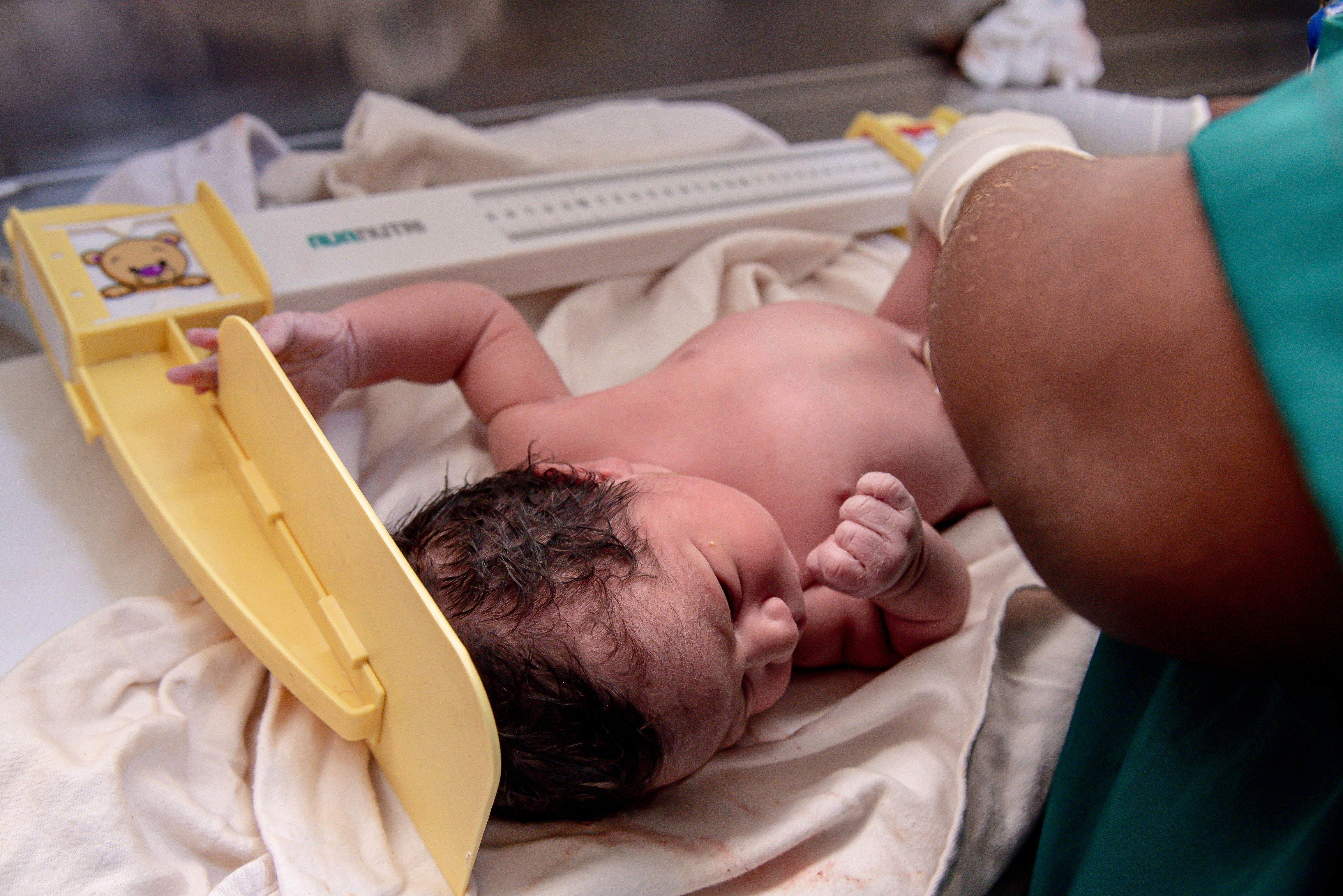 A newborn baby is weighed by a healthcare worker in a hospital setting. Captured close-up.
