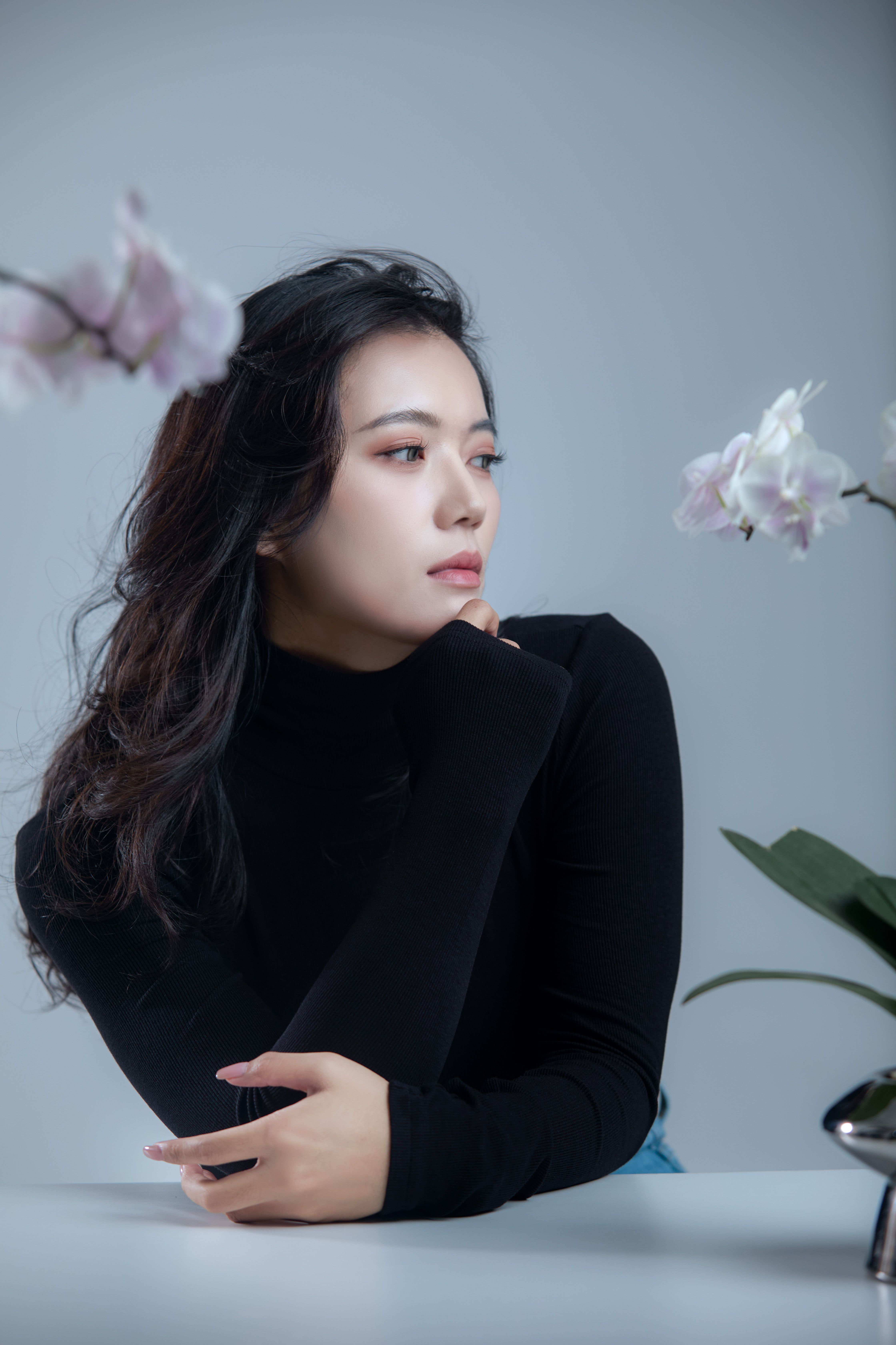 Stylish woman in a black top poses with white orchids in a serene setting.