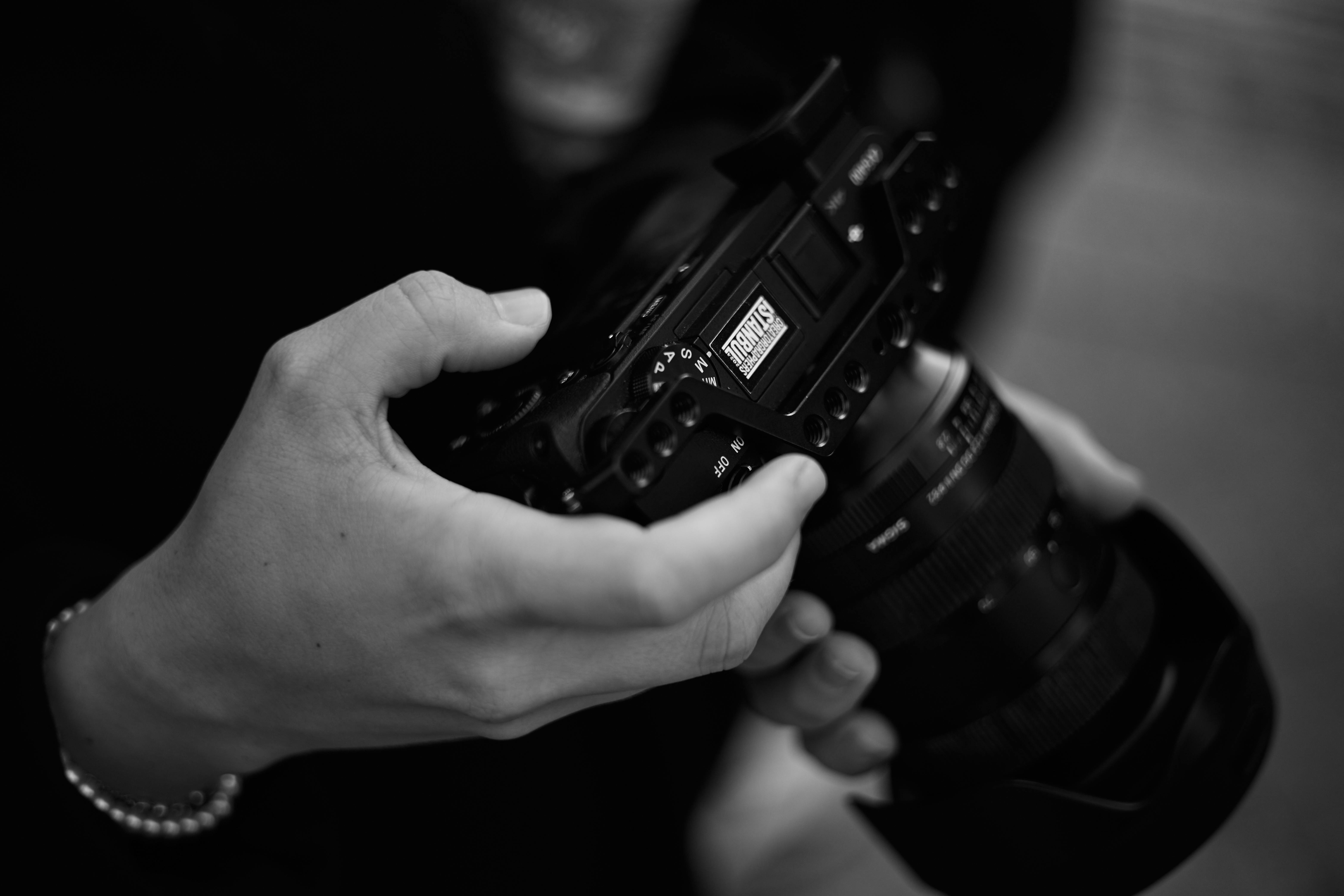Gratis Le mani di un fotografo professionista impugnano una fotocamera DSLR, mostrando precisione e messa a fuoco in bianco e nero. Foto a disposizione