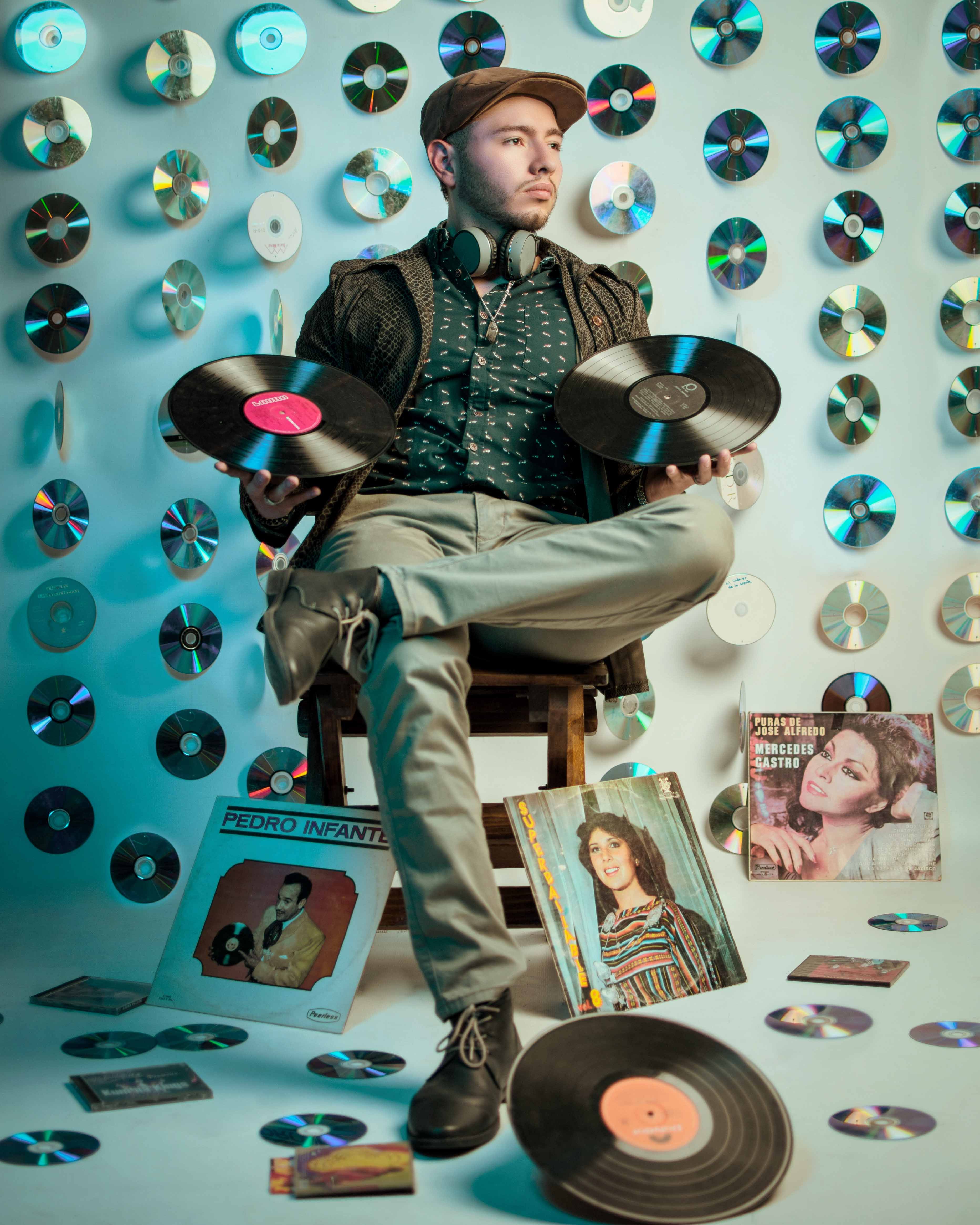 Young man with headphones poses with vinyl records amidst a retro music collection.