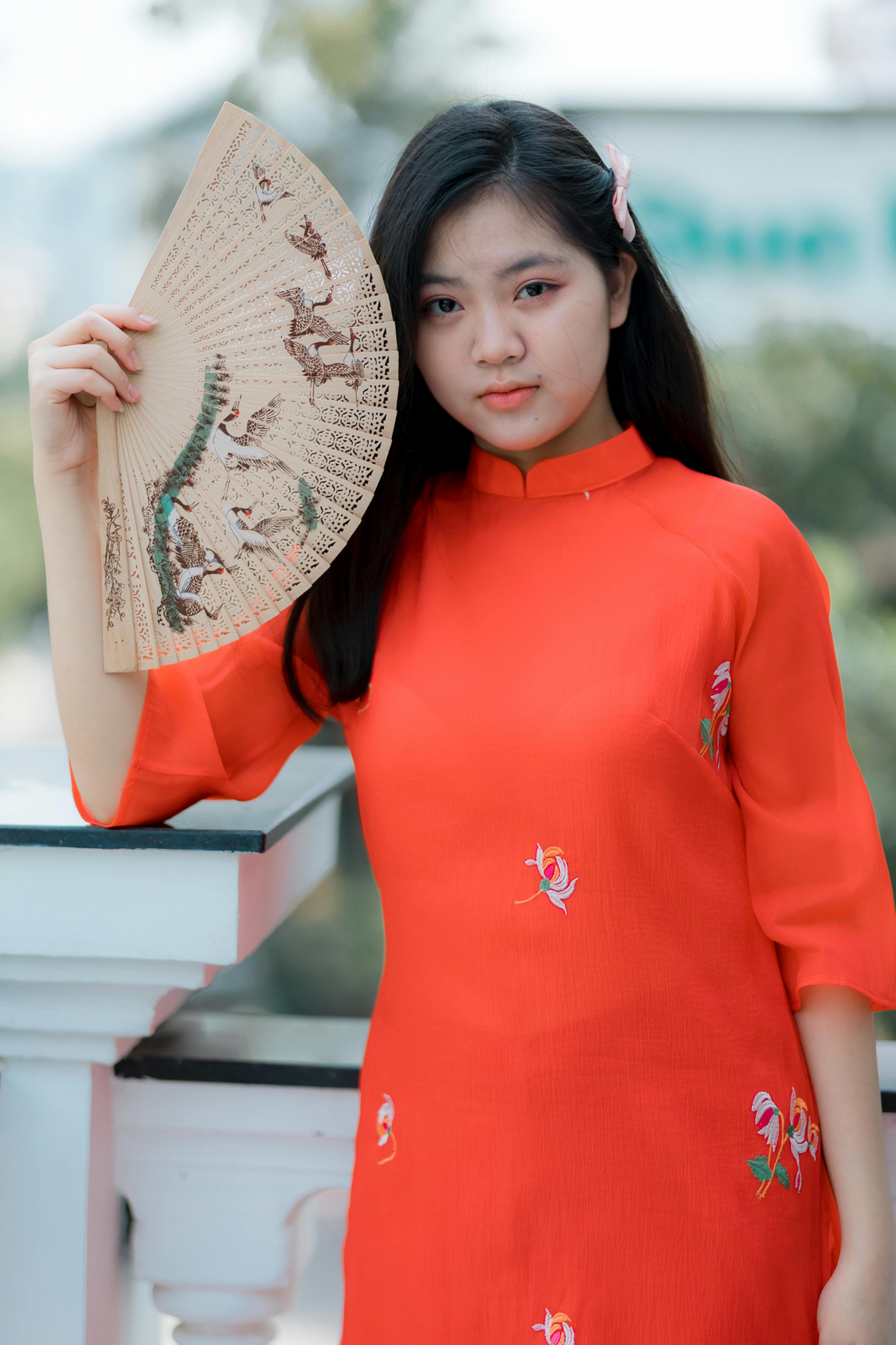 Portrait of a young woman wearing a red Ao Dai and holding a traditional fan outdoors.