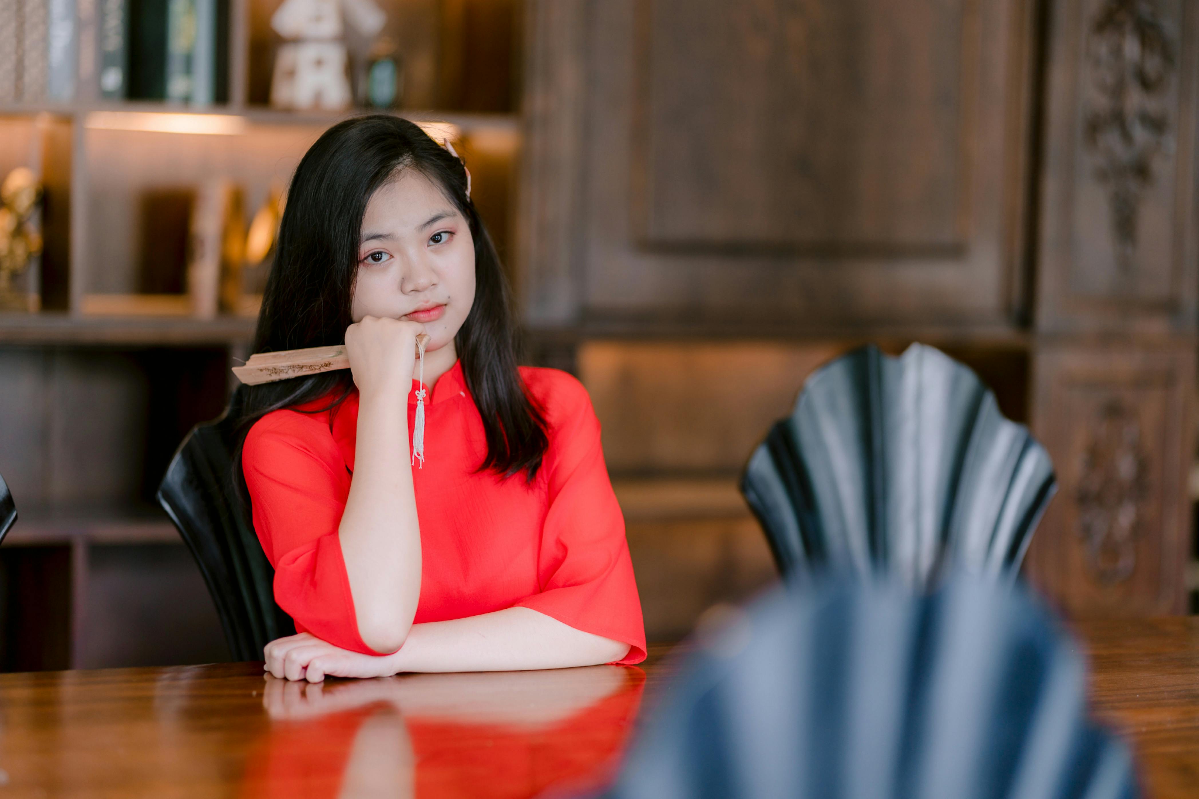 Ilmainen Nuori nainen kirkkaanpunaisessa mekossa istuu mietteliäänä sisätiloissa. Kuvapankkikuva