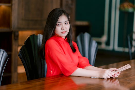 Young woman in traditional red dress sitting at a table indoors.