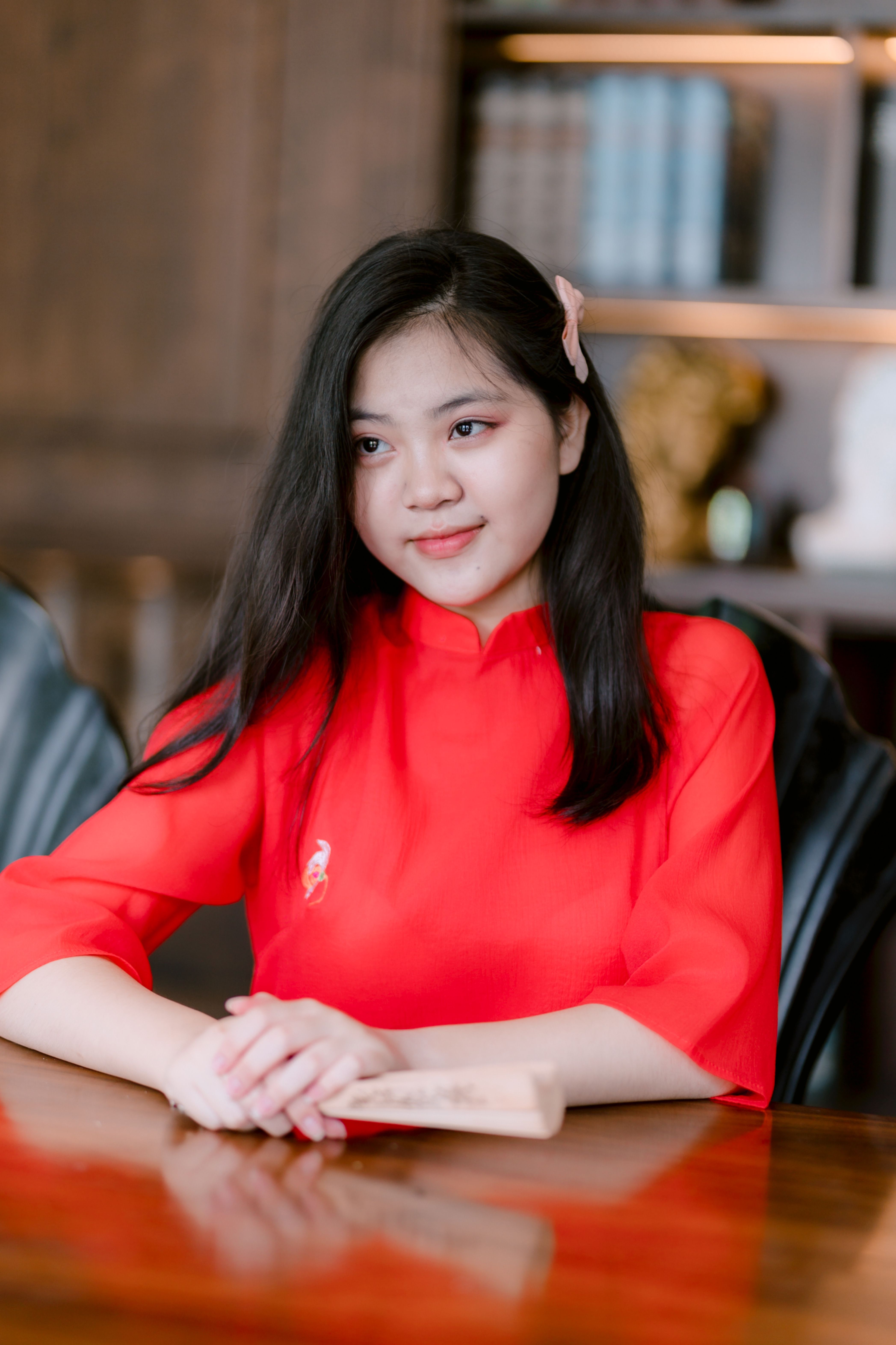 Young woman in red traditional dress seated indoors, looking contemplative.
