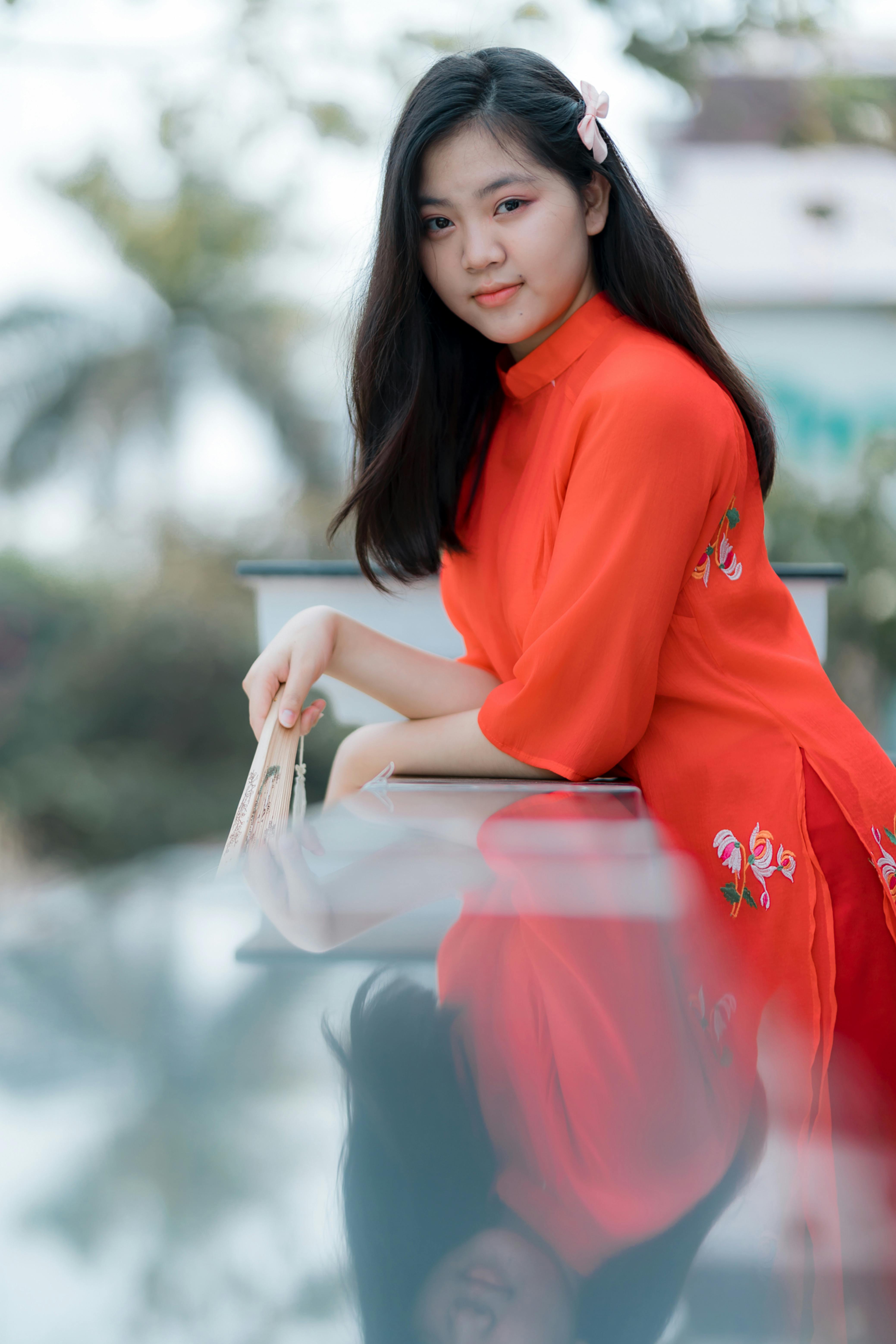Elegant woman in red dress posing outdoors with serene expression.