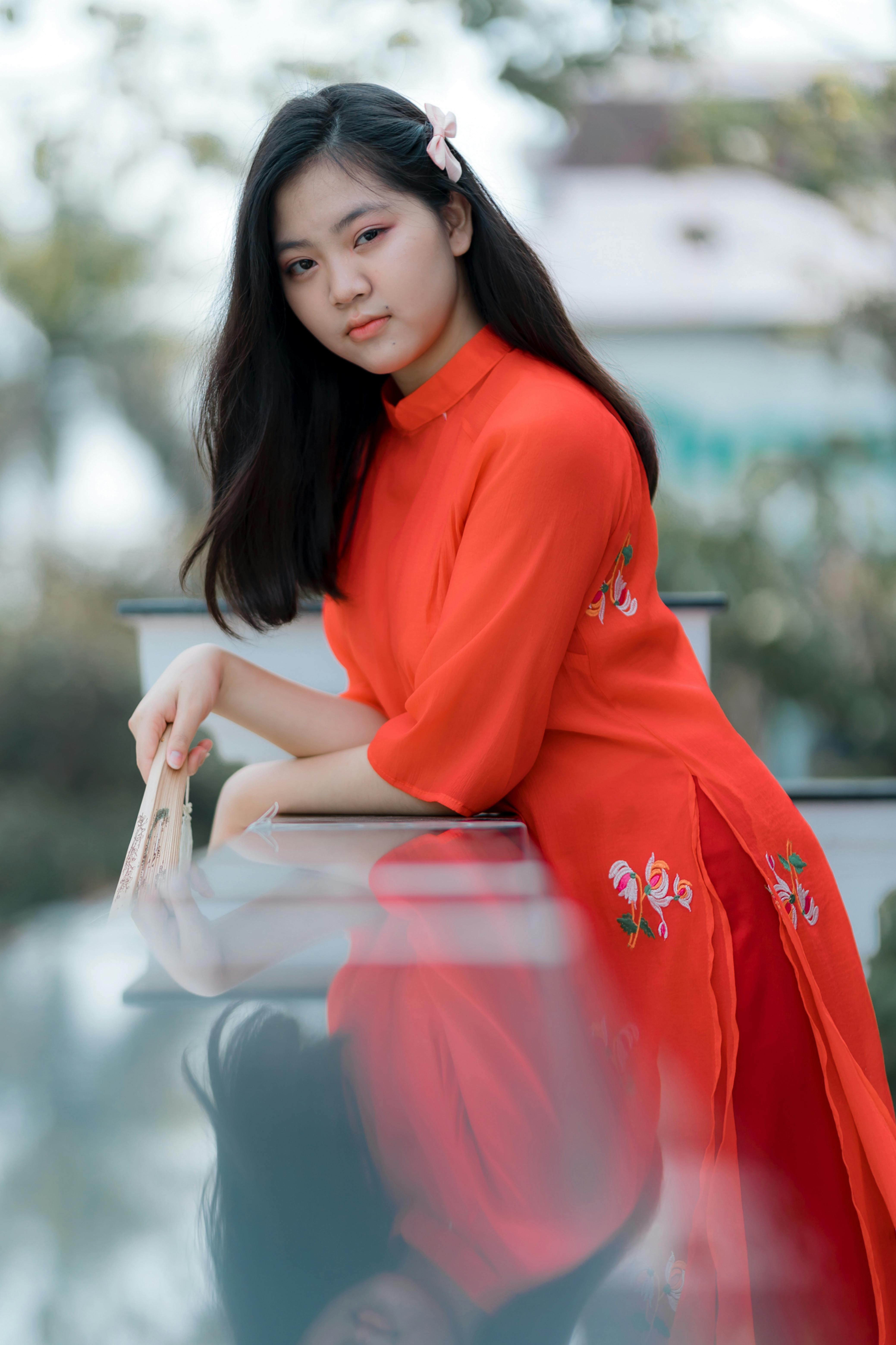 Young woman in a bright red traditional dress, posing outdoors with a serene expression.