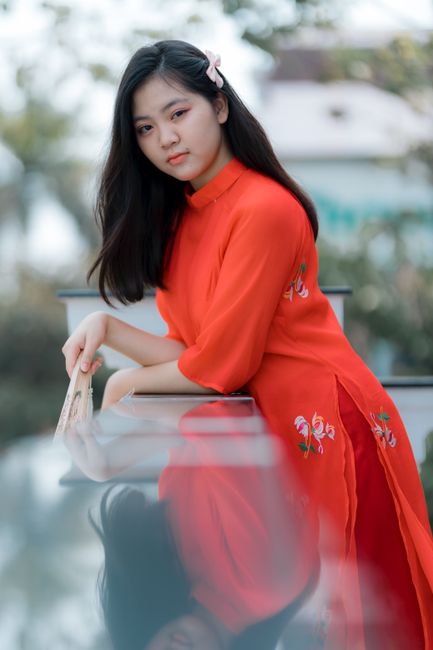 Young woman in a bright red traditional dress, posing outdoors with a serene expression.