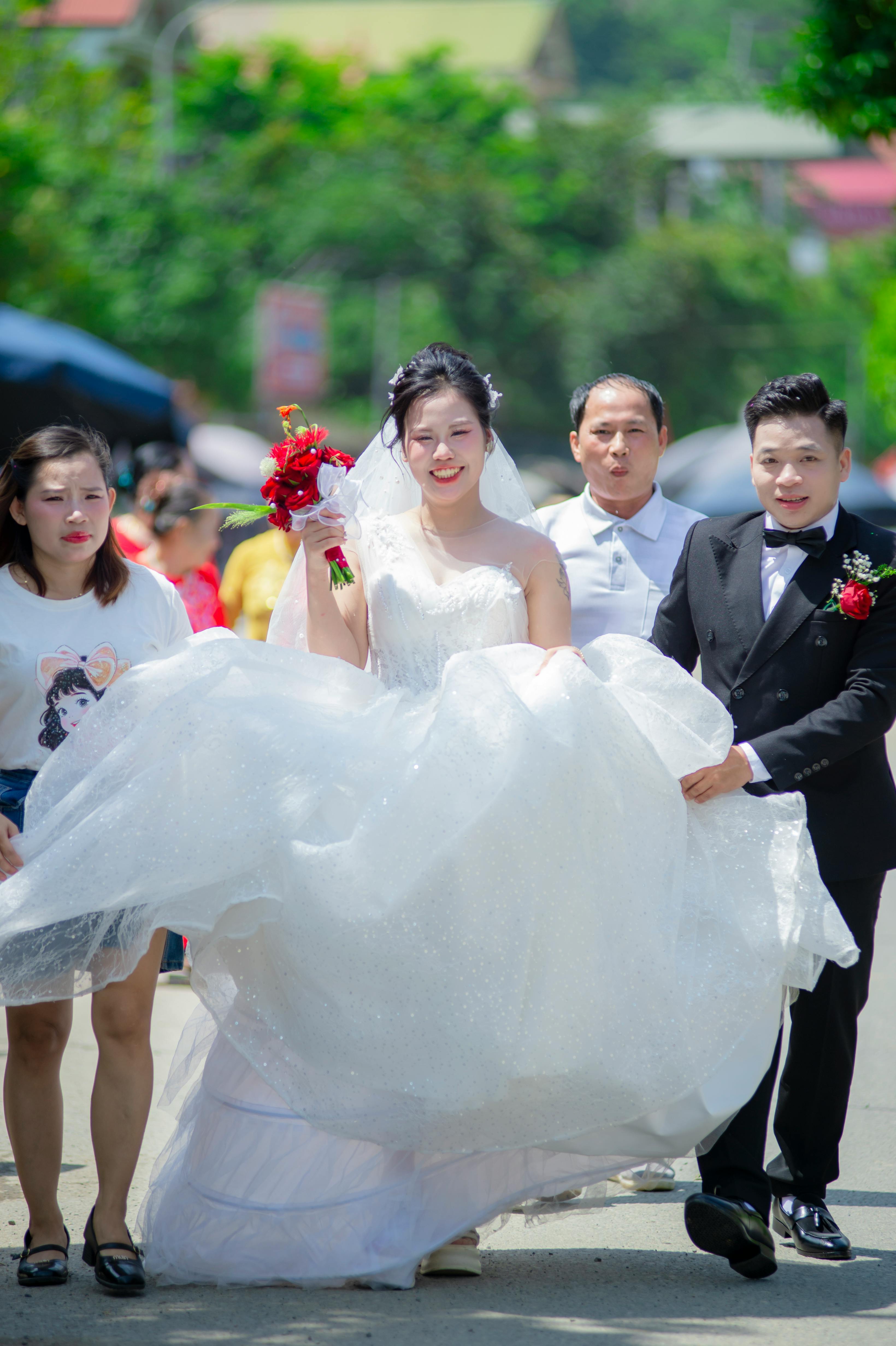 Gratis Prosesi pernikahan Vietnam yang penuh sukacita, dengan sang pengantin wanita mengenakan gaun yang memukau, dikawal ke luar ruangan pada hari yang cerah. Foto Stok