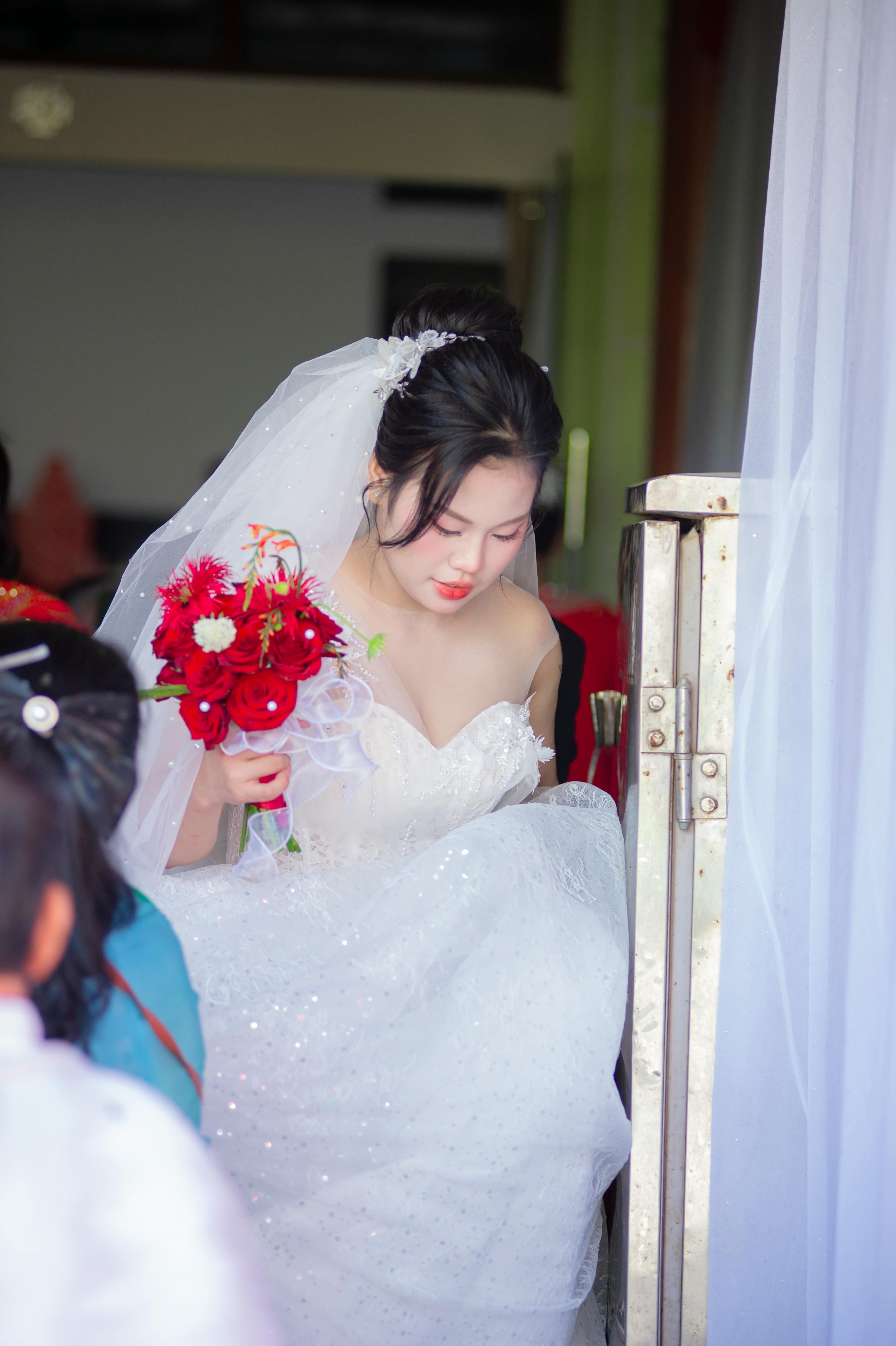 De franc Una bonica núvia vietnamita amb un vestit blanc que sosté un ram vermell vibrant, que simbolitza l'elegància i l'alegria. Foto d'estoc