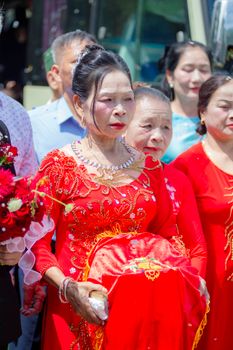 Elderly women in vibrant red dresses participate in a traditional Vietnamese wedding ceremony.