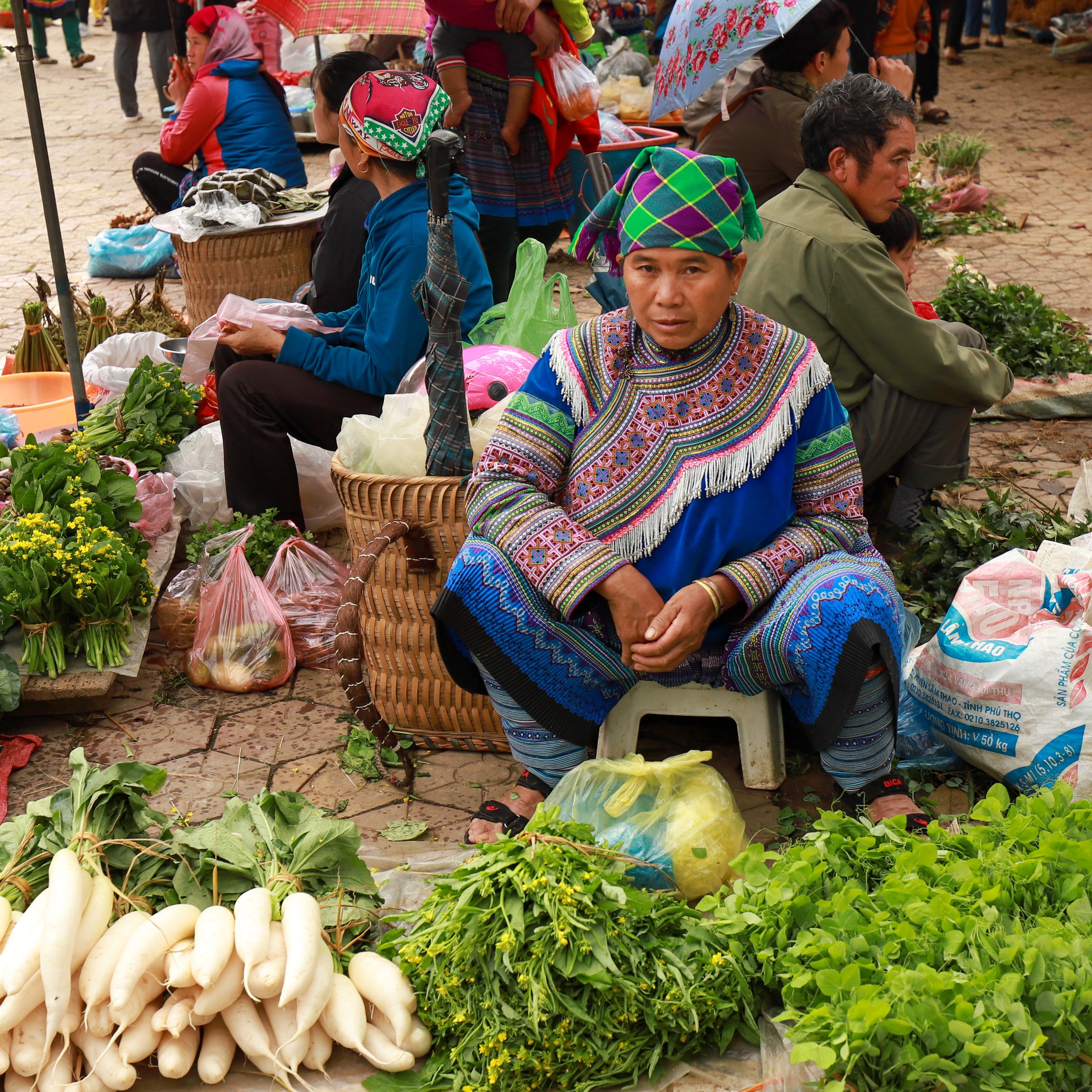 Colorful traditional market scene in Lào Cai, Việt Nam, featuring a Hmong vendor with fresh produce.