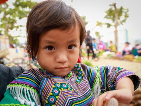 Close-up portrait of an ethnic child in traditional attire at a vibrant market in Lào Cai, Vietnam.