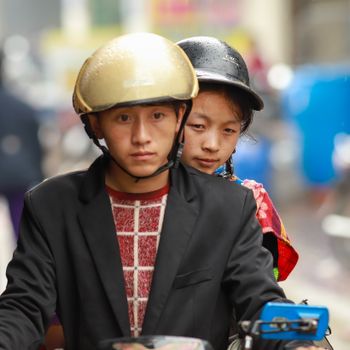 Two young people riding a motorbike on a rainy day in Lào Cai, showcasing urban life.