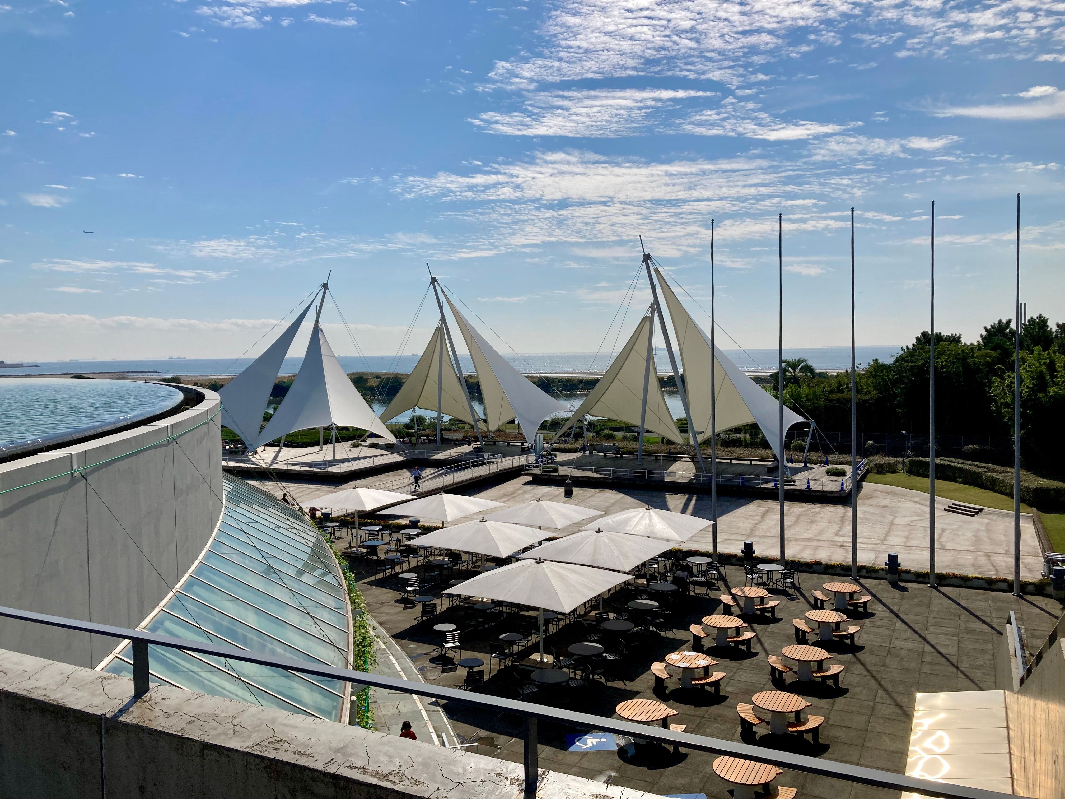 Moderne Terrasse mit straff gespanntem Sonnensegel über einem Esstisch in hellen Beigetönen