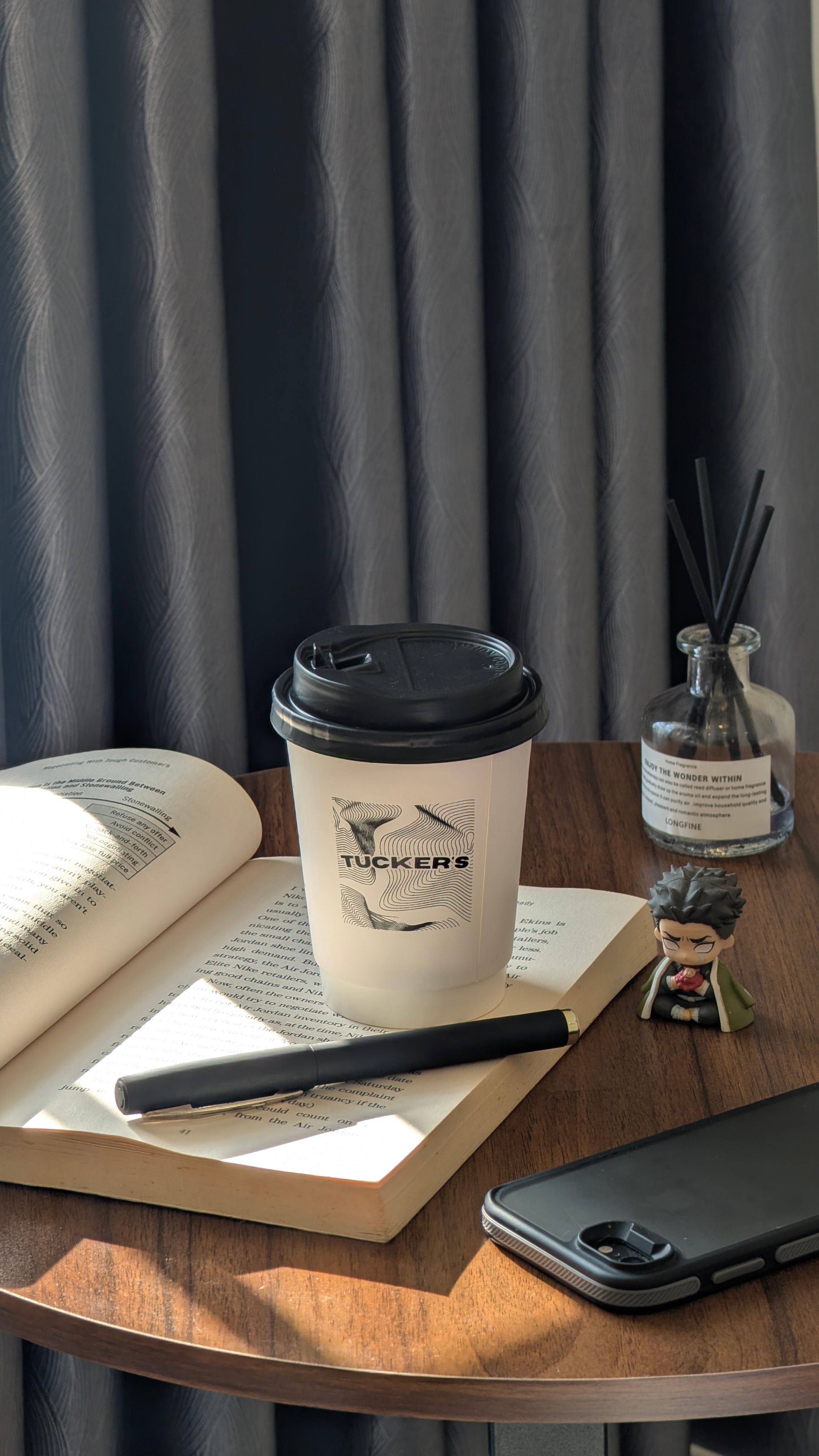 Relaxing setup with a coffee cup, book, and smartphone on a table, perfect for a cozy break.