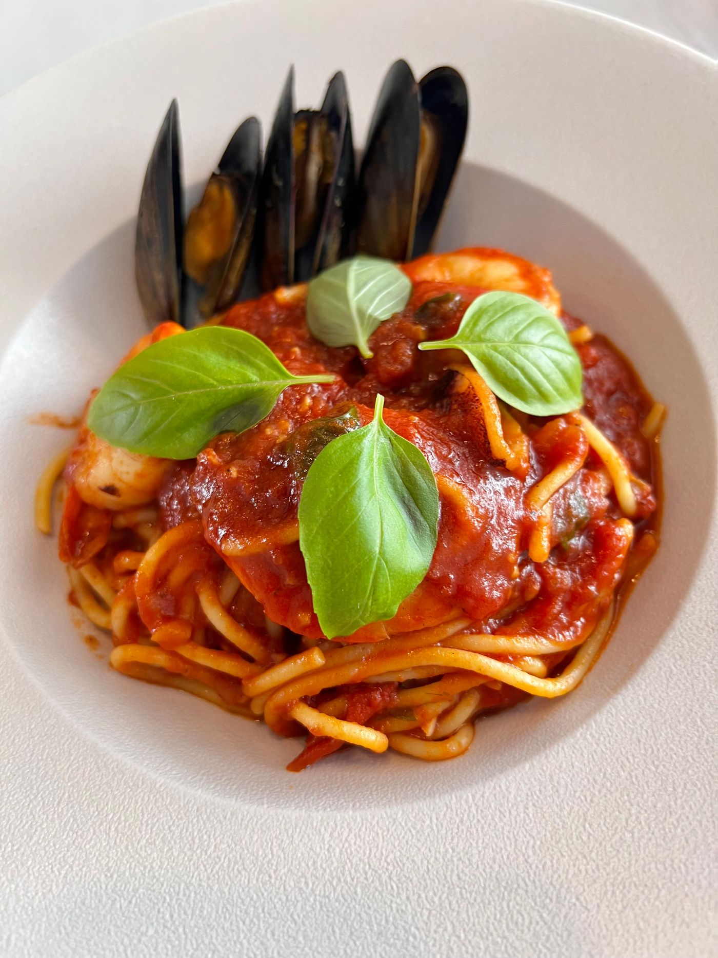 Spaghetti con cozze, pomodoro e basilico in una scodella bianca