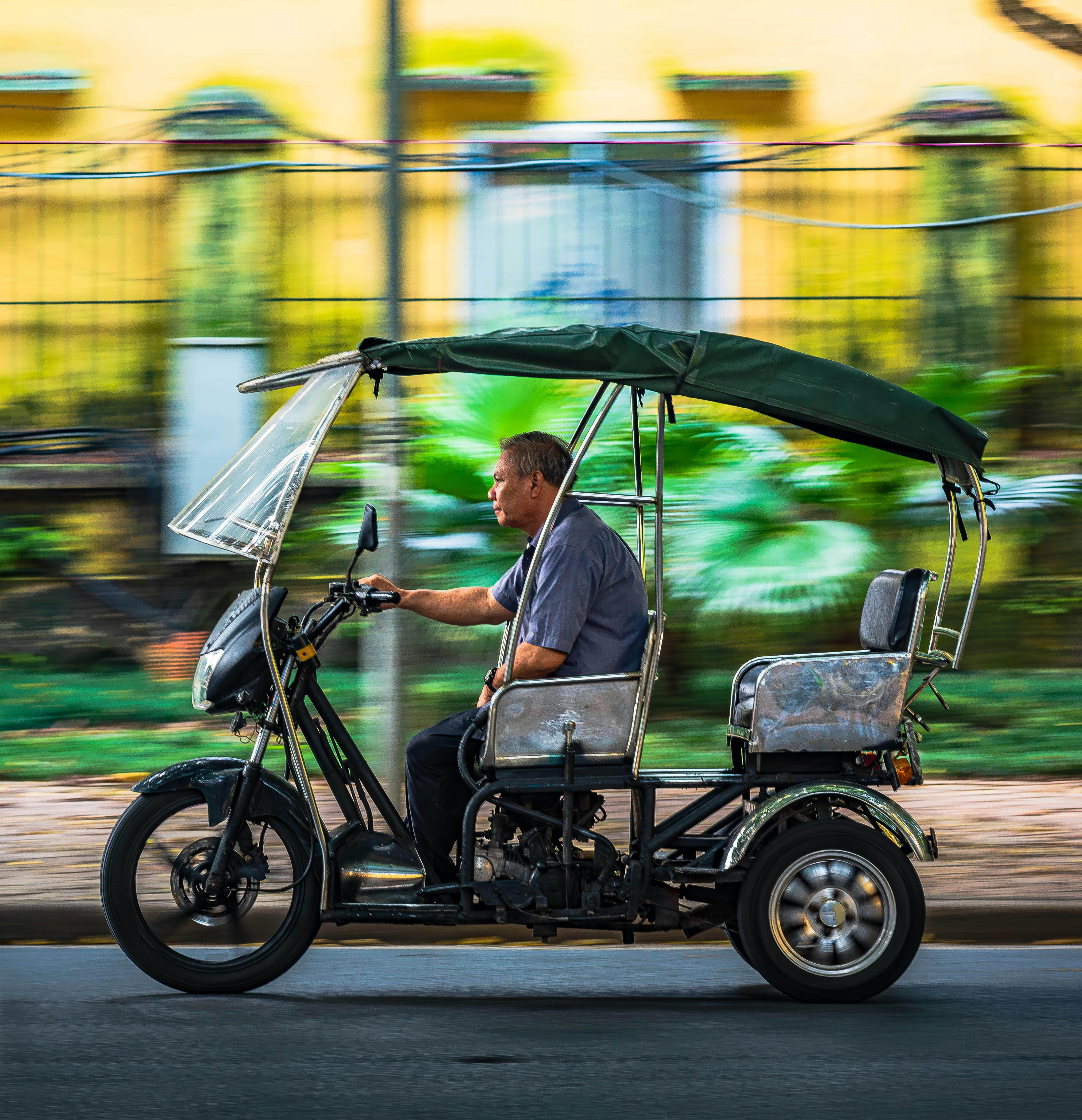 Free A man driving a motorized tricycle with a canopy, captured in motion blur on a city street. Stock Photo