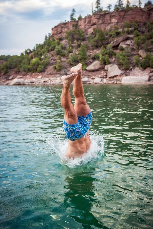 Free A man performs a skilled dive into a lake, surrounded by scenic cliffs and clear water. Stock Photo