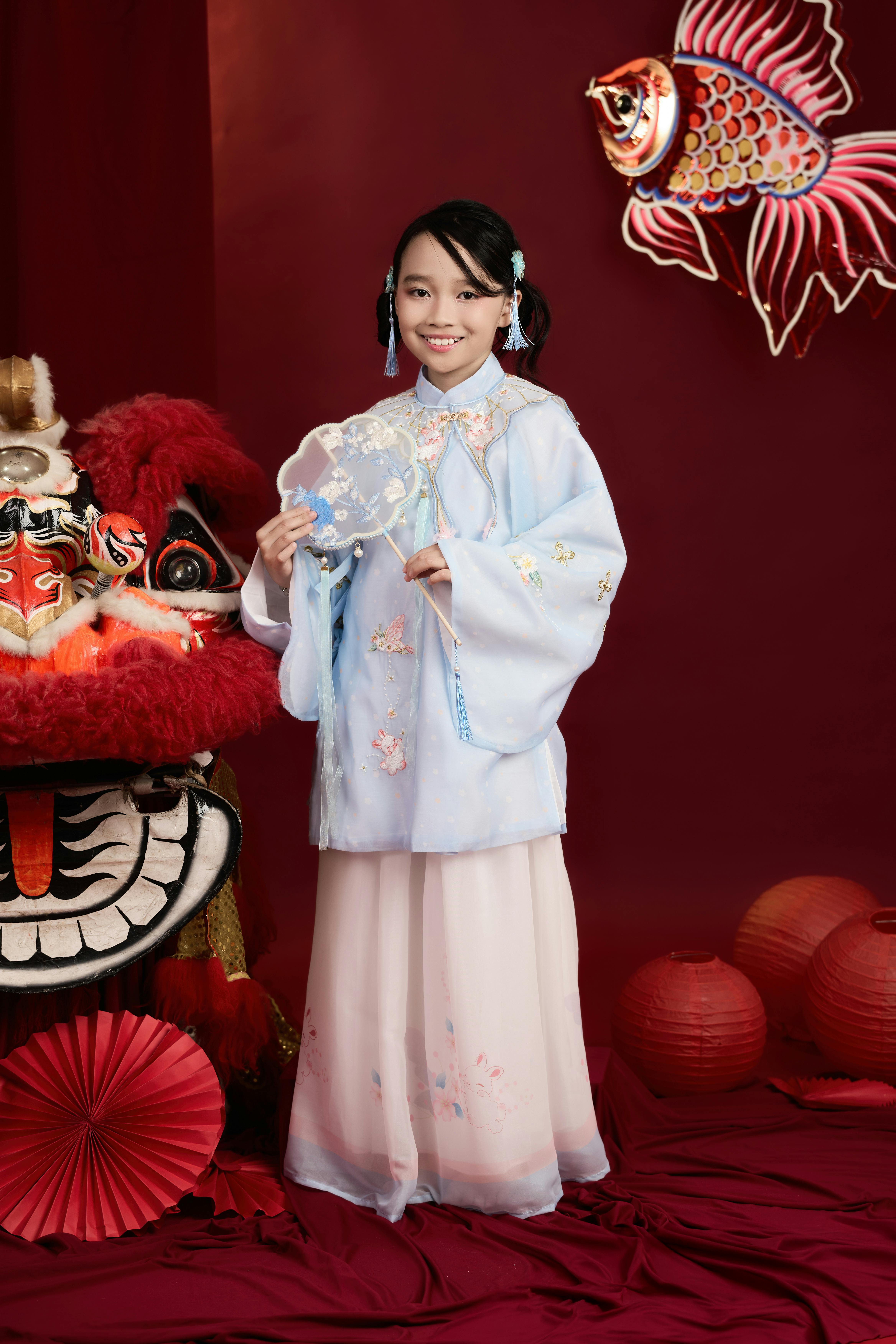 Miễn phí Một cô gái trẻ trong trang phục truyền thống đón Tết Nguyên đán trong bối cảnh sôi động với đèn lồng đỏ và trang phục múa lân. Ảnh lưu trữ