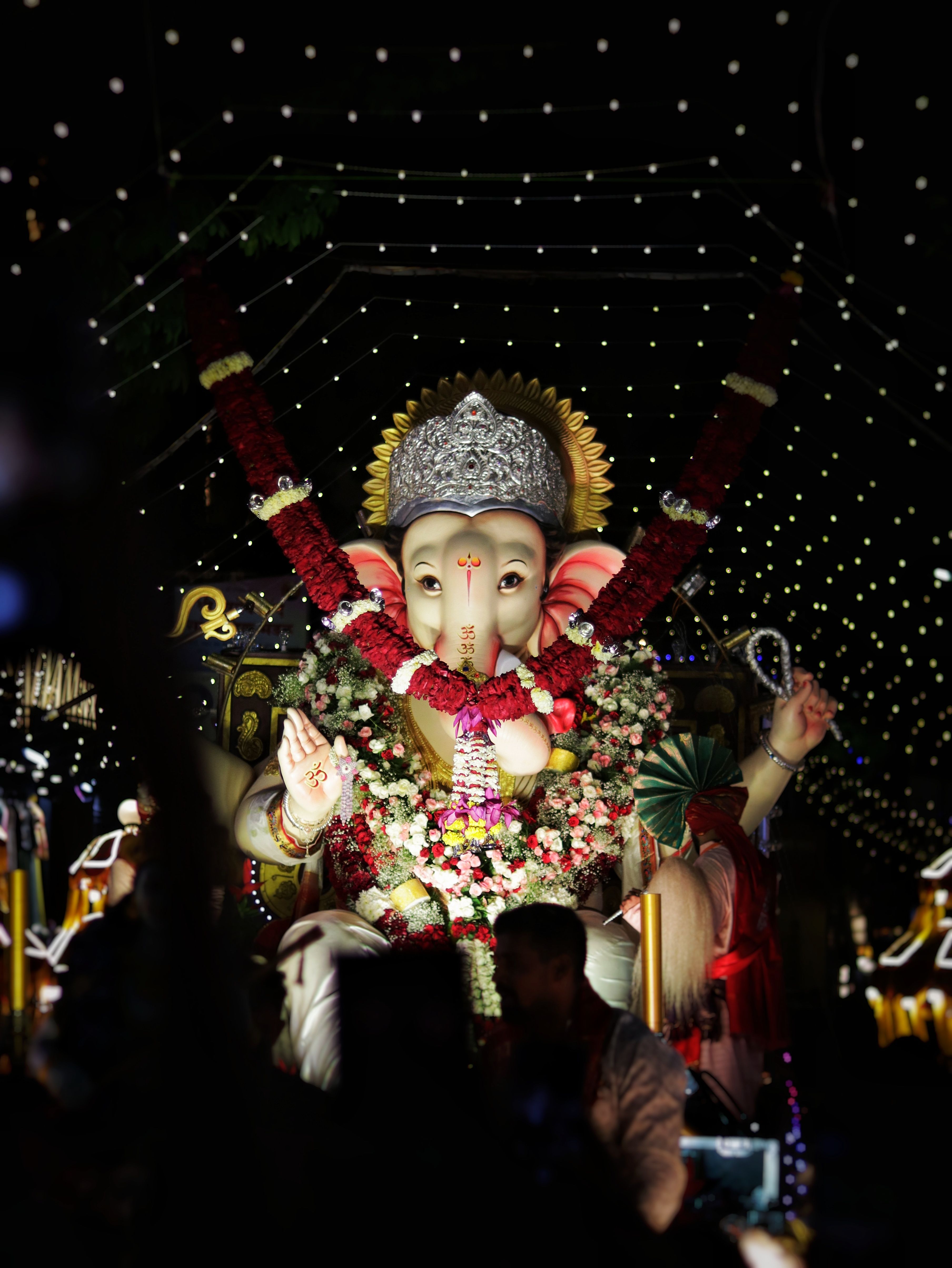 Illuminated Ganesh idol adorned with flowers during a vibrant nighttime festival celebration.