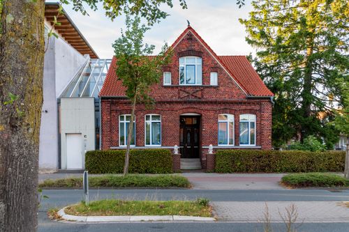 Free Red brick house with triangular roof and white-trimmed windows, surrounded by greenery. Stock Photo