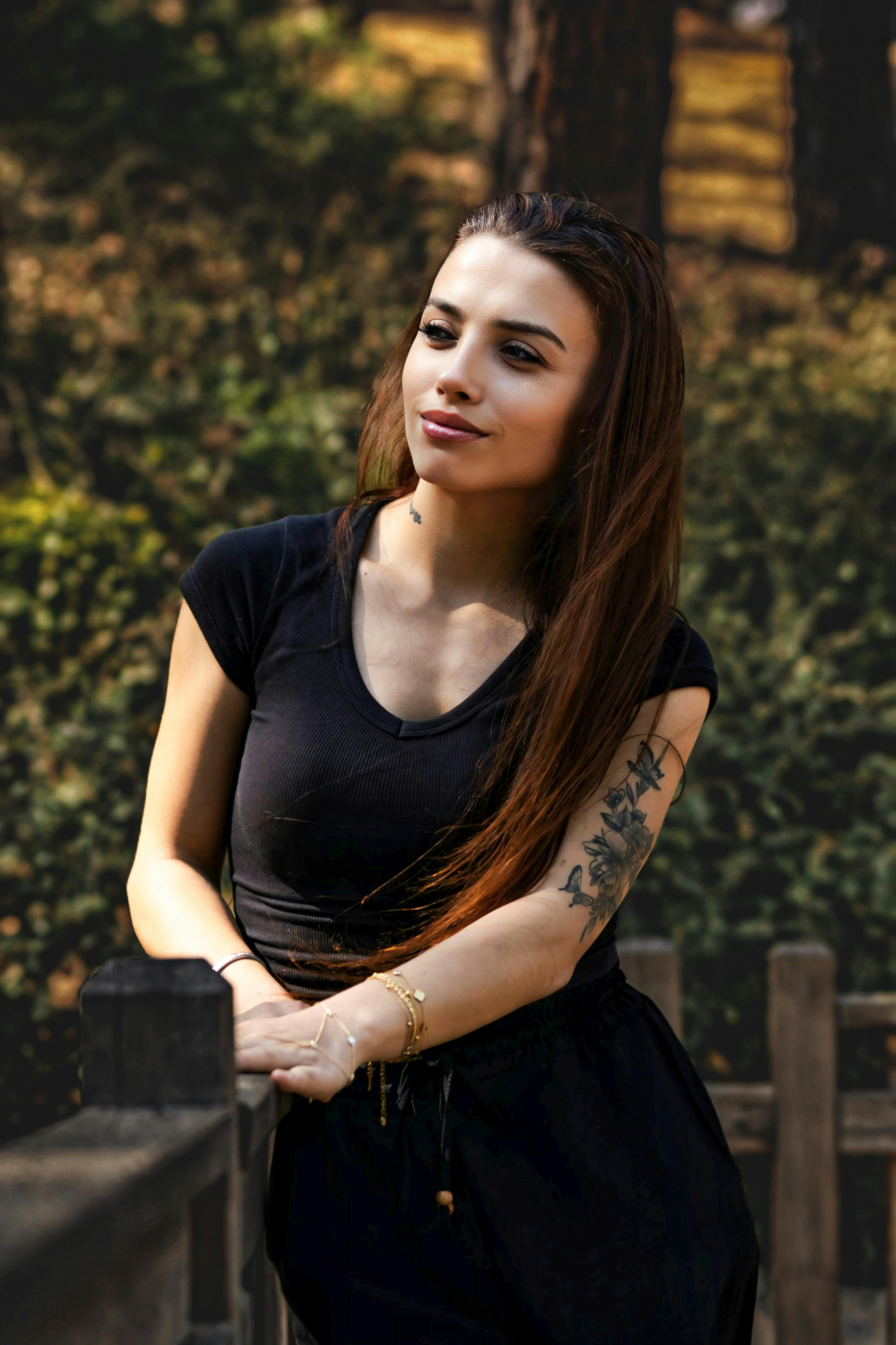 A young woman with tattoos leaning on a wooden rail, enjoying a sunny day outdoors.