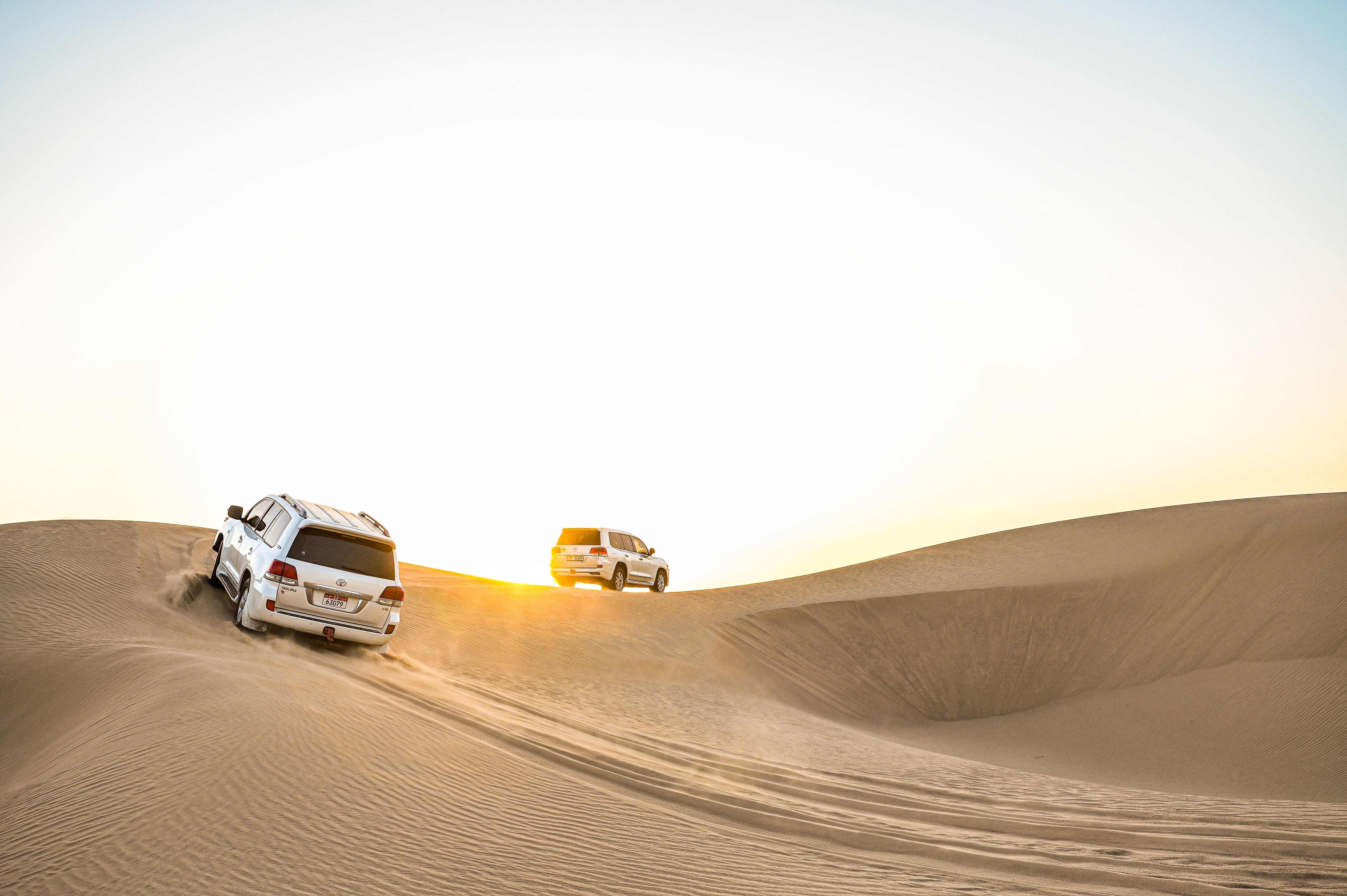 White SUVs navigating the golden dunes at sunset in Sweihan, Abu Dhabi.