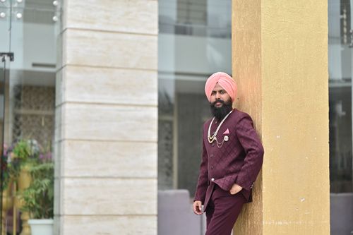 Free Stylish man in maroon attire with turban and accessories leaning against a gold column outdoors. Stock Photo