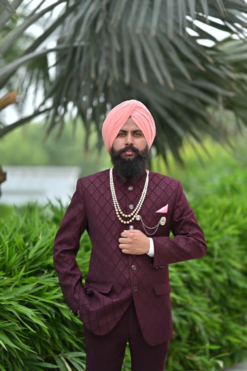 Free A stylish Sikh man in a burgundy suit and pink turban posing outdoors with lush greenery. Stock Photo