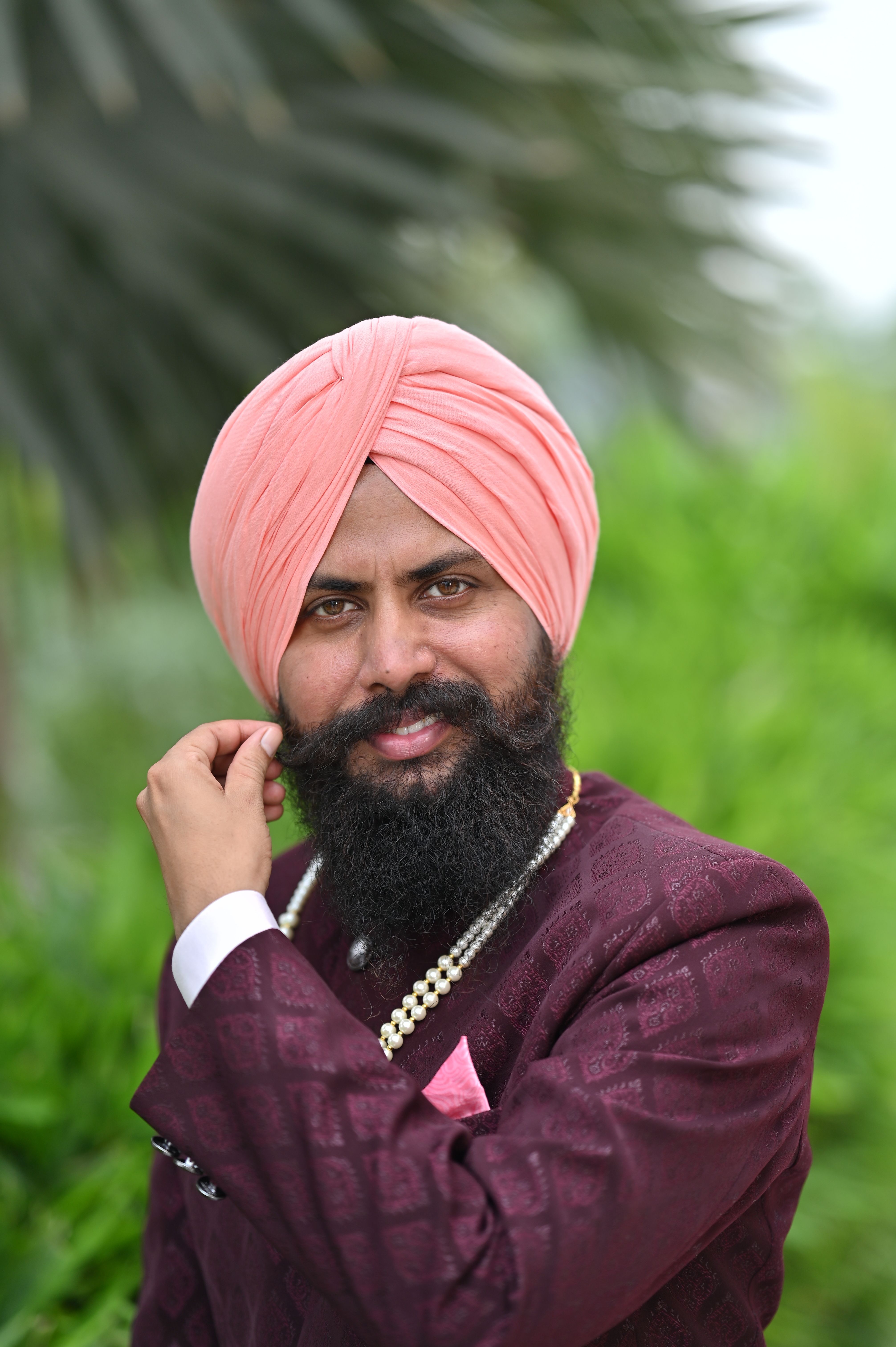 A striking portrait of a bearded man in elegant traditional attire with a pink turban, outdoors.