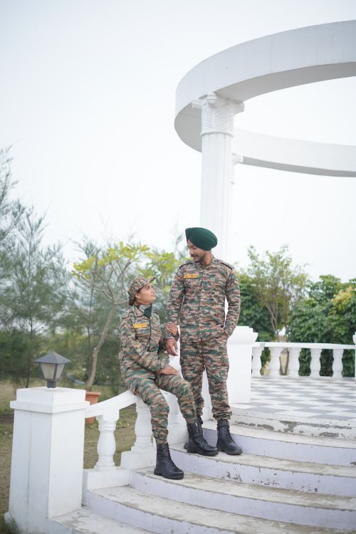 Free Two military personnel in camouflage uniforms outdoors on stairs near a white structure. Stock Photo