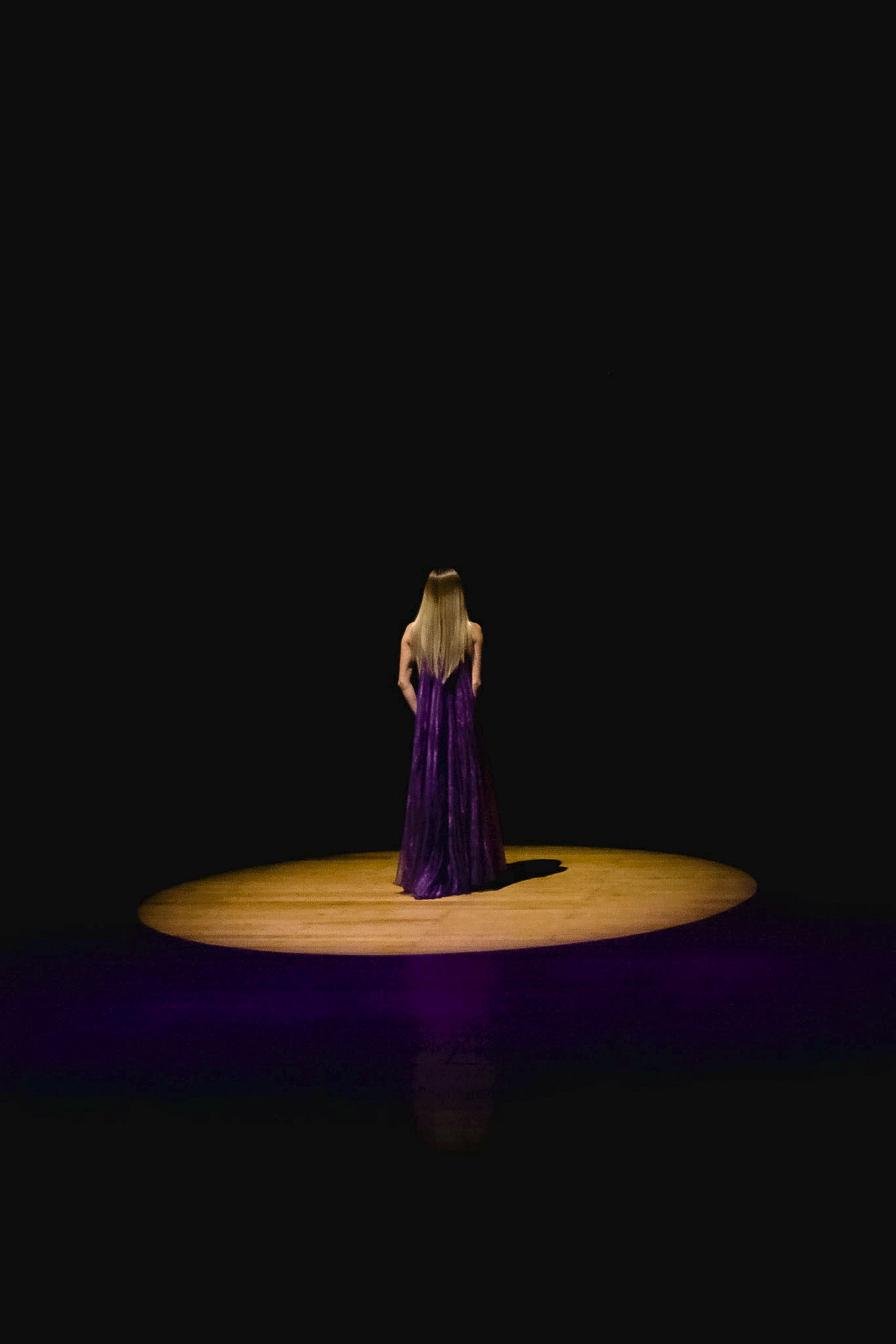 De franc Dona elegant amb vestit morat dret sobre un escenari amb focus. Dramàtica i artística. Foto d'estoc