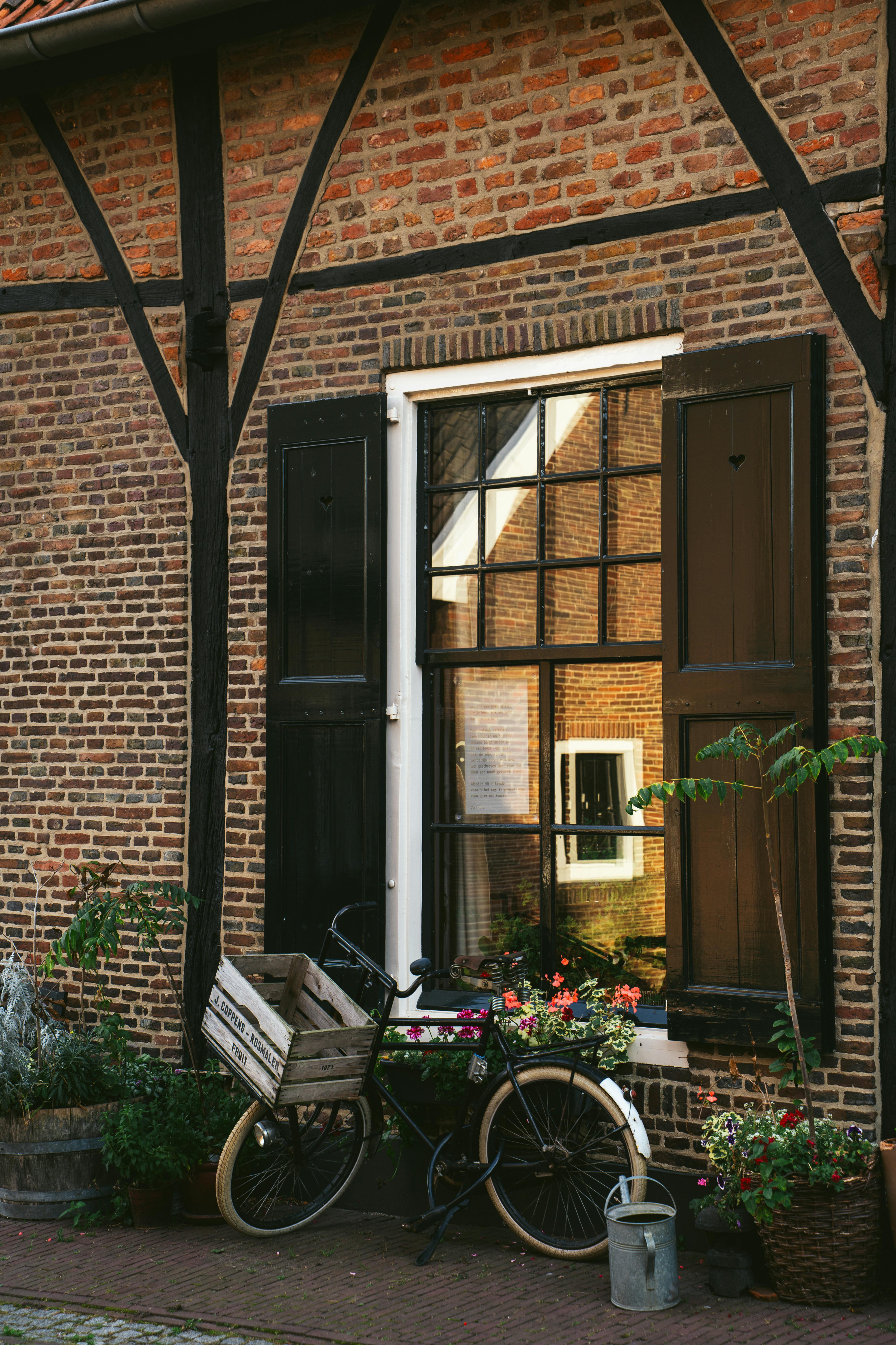 A vintage bicycle rests against a rustic brick wall adorned with flowers, reflecting a charming and peaceful afternoon scene.