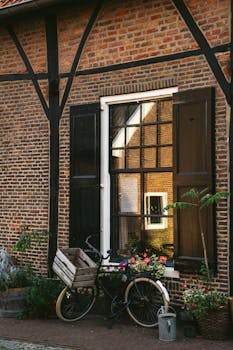A vintage bicycle rests against a rustic brick wall adorned with flowers, reflecting a charming and peaceful afternoon scene.