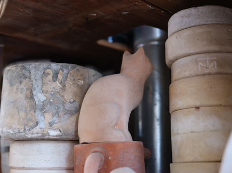 A clay cat sculpture placed among various stacked stone pots in a rustic setting.