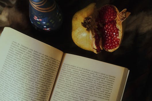 Stylish composition of an open book, pomegranate, and vase with natural lighting.