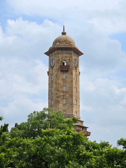 Free Historic clock tower in Ahmedabad, India, framed by lush greenery under a blue sky. Stock Photo
