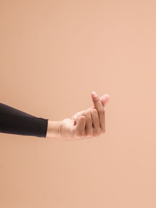 Free A close-up of a hand making a heart gesture against a warm beige background. Stock Photo