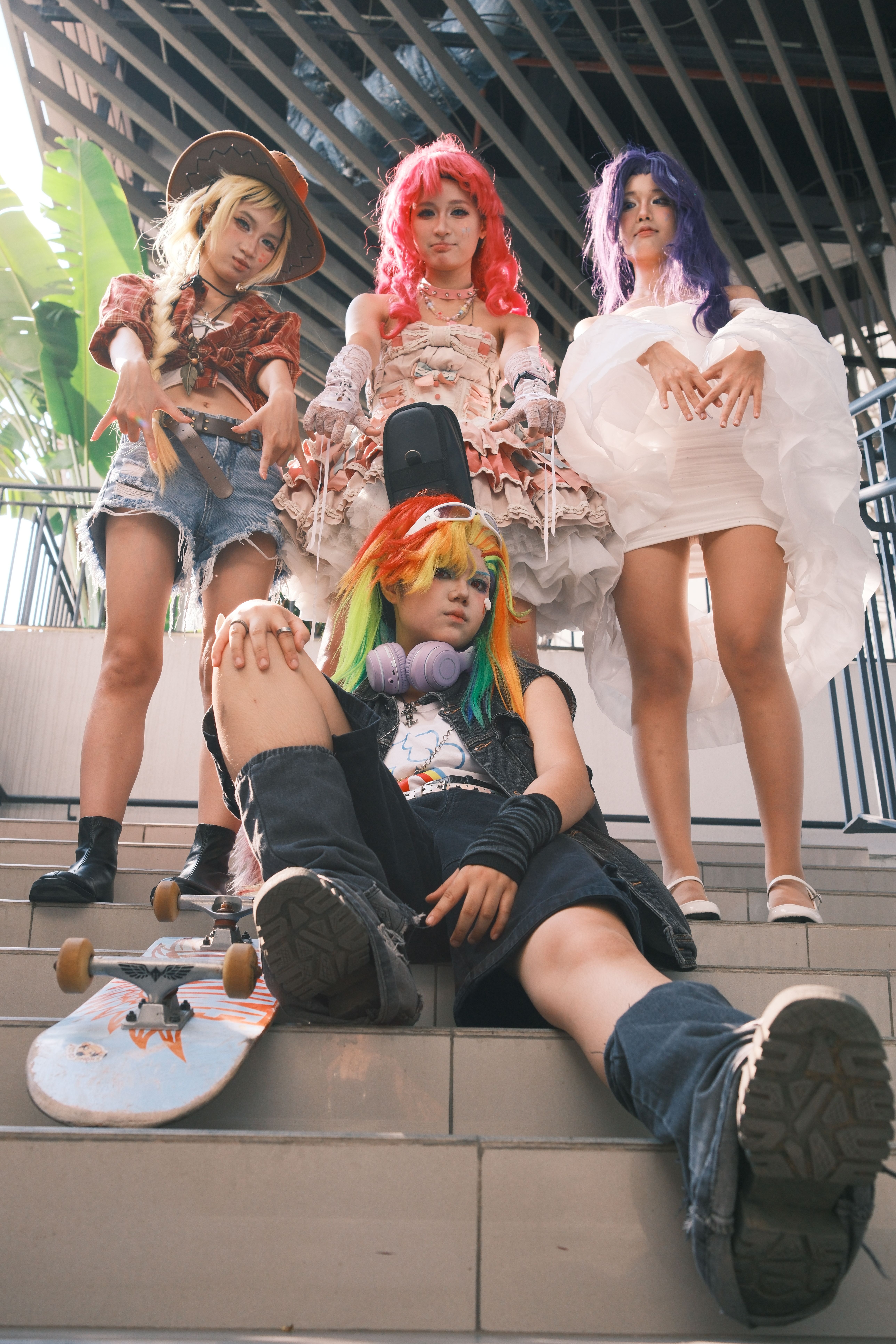 A group of four young adults in colorful cosplay attire sit and stand on stairs.